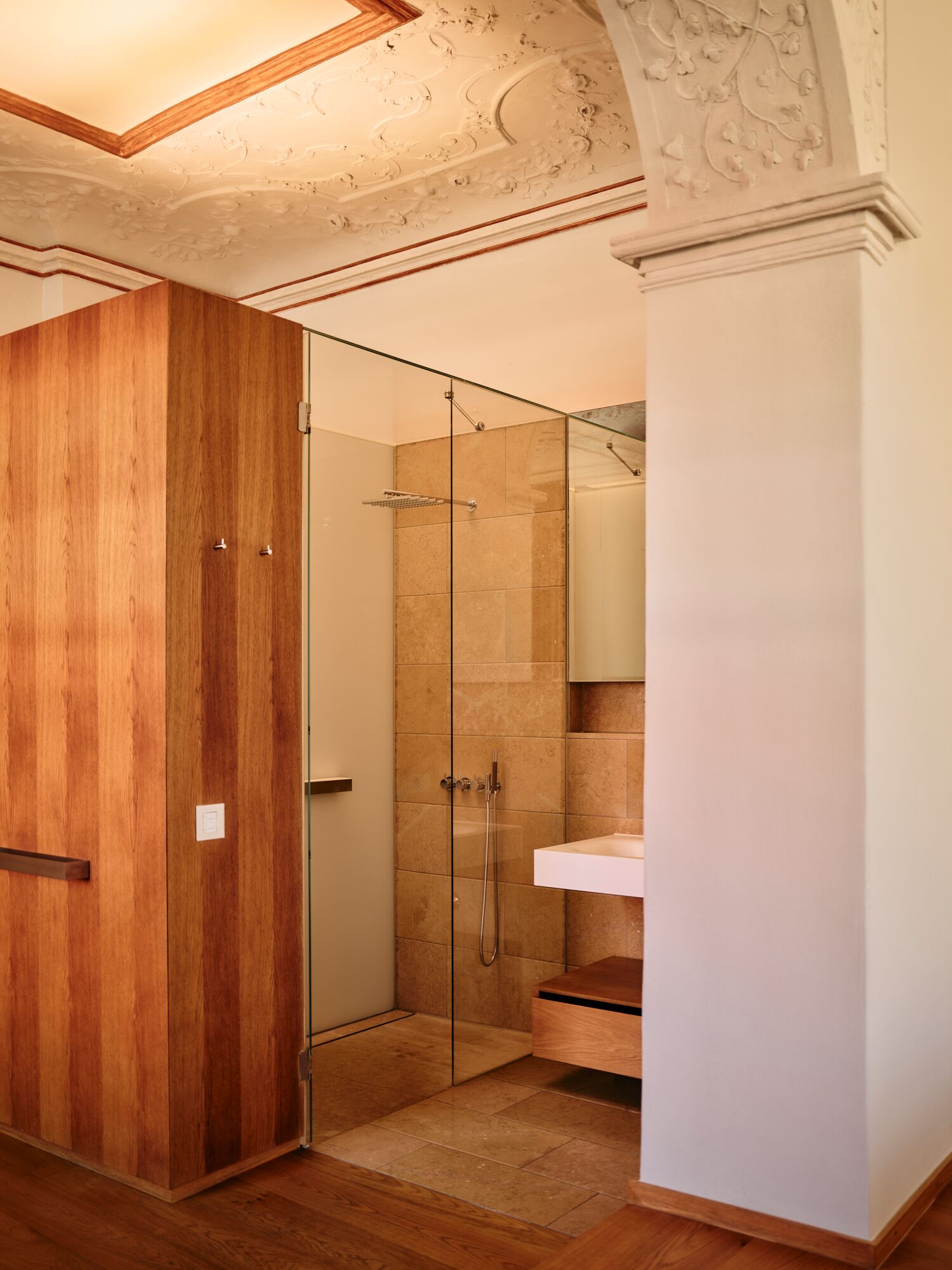 A modern bathroom with a wooden wardrobe, a glass shower enclosure, and a white sink.