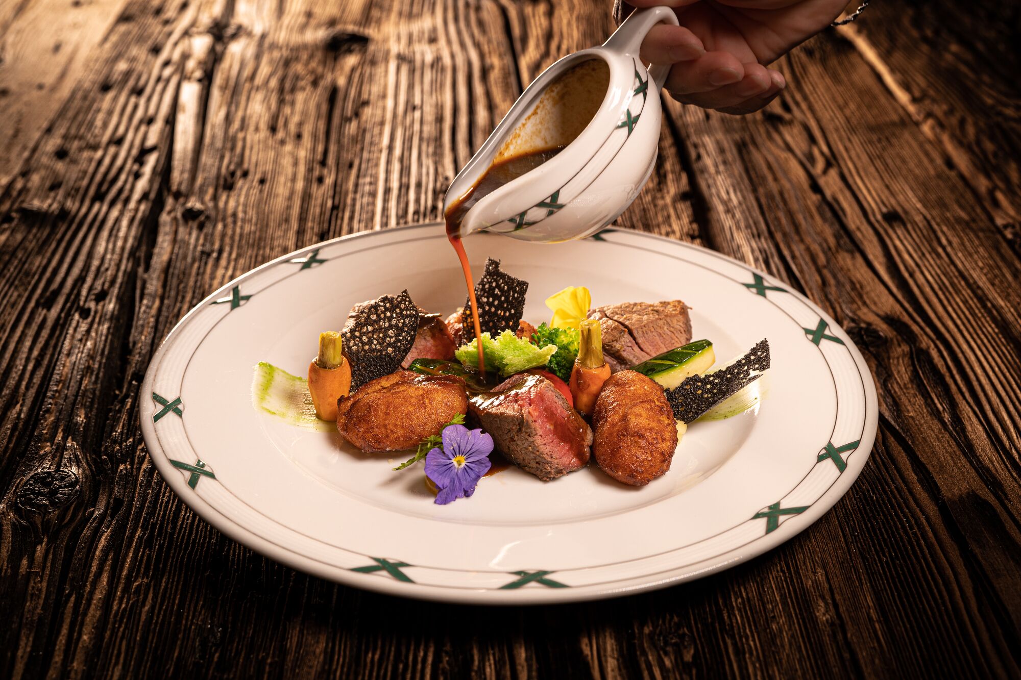 Un plato de comida con diferentes carnes y verduras, salsa siendo vertida, y un rústico fondo de mesa de madera.
