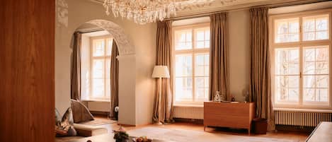 A spacious living room with a chandelier, large windows, a sofa, a coffee table, and a wooden cabinet.
