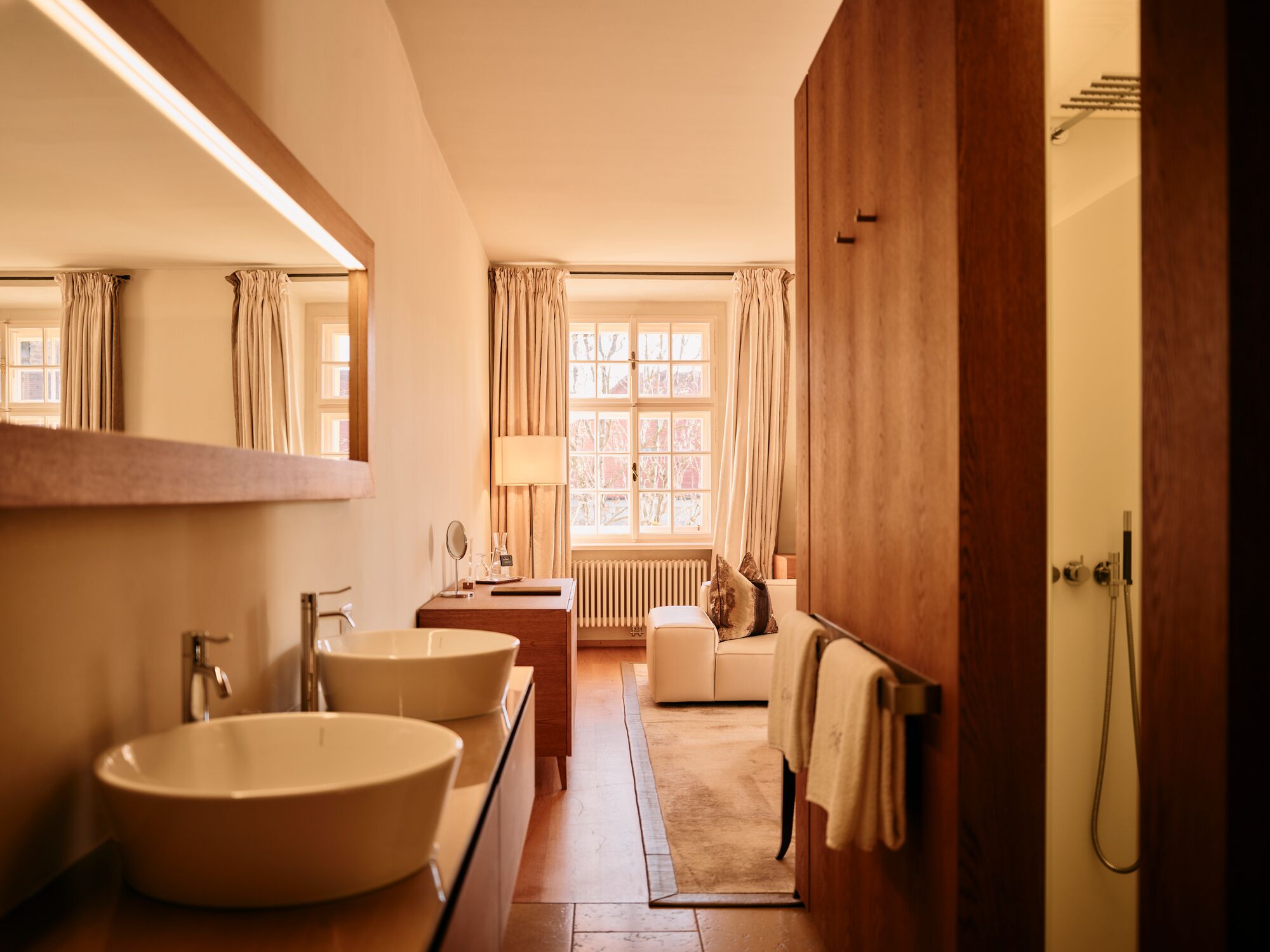 A bathroom with two sinks, a mirror, a towel rack, a window with curtains, and a shower area.