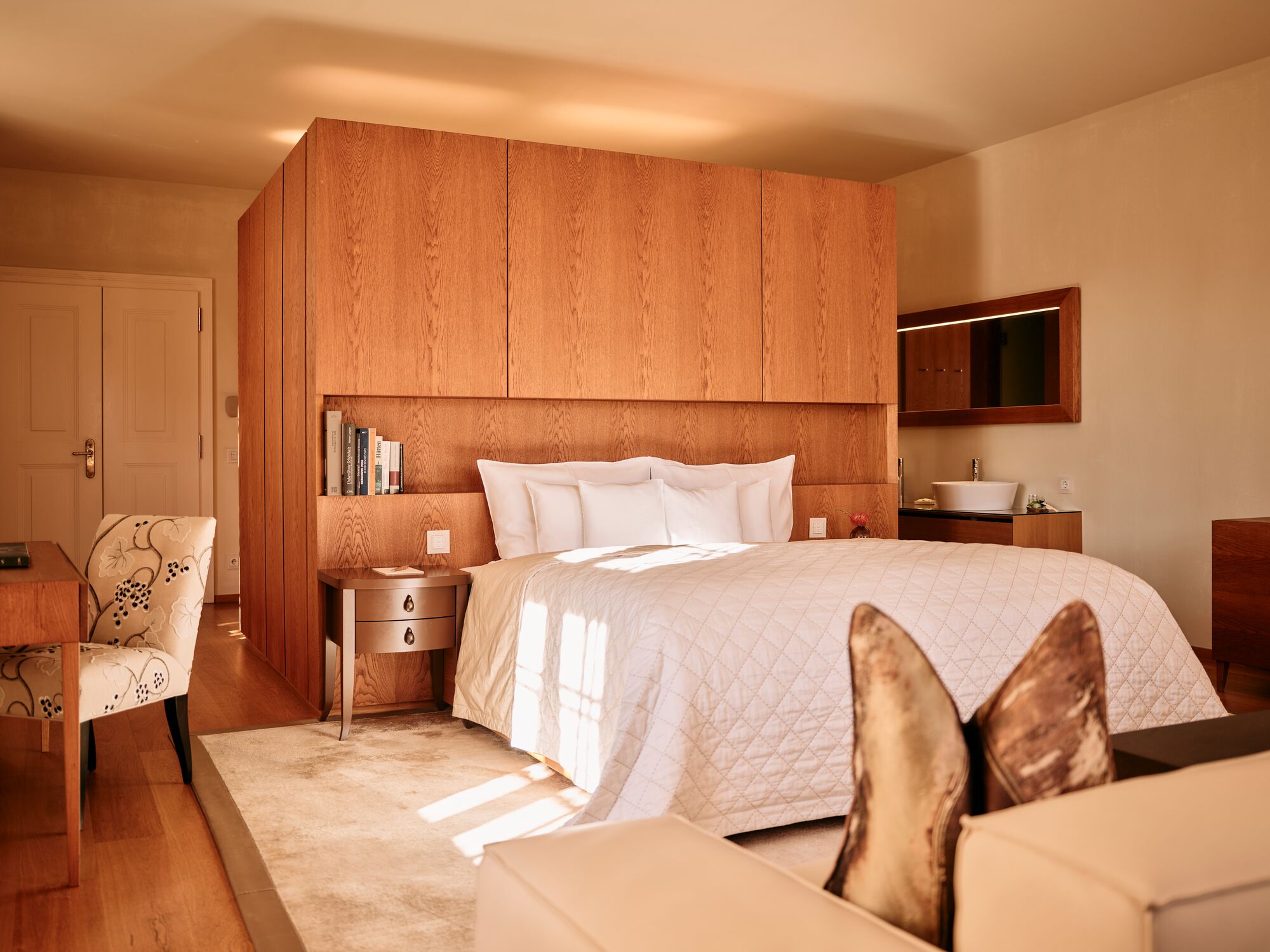 Un dormitorio con una cama grande, cabecera de madera, mesitas de noche, una silla y un espejo.