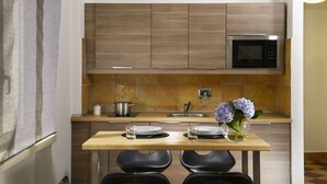 A modern kitchen with wooden cabinets, a stainless steel microwave, and a dining area with two black chairs and a table set with plates and glasses. - Maison Re di Roma (Rome)