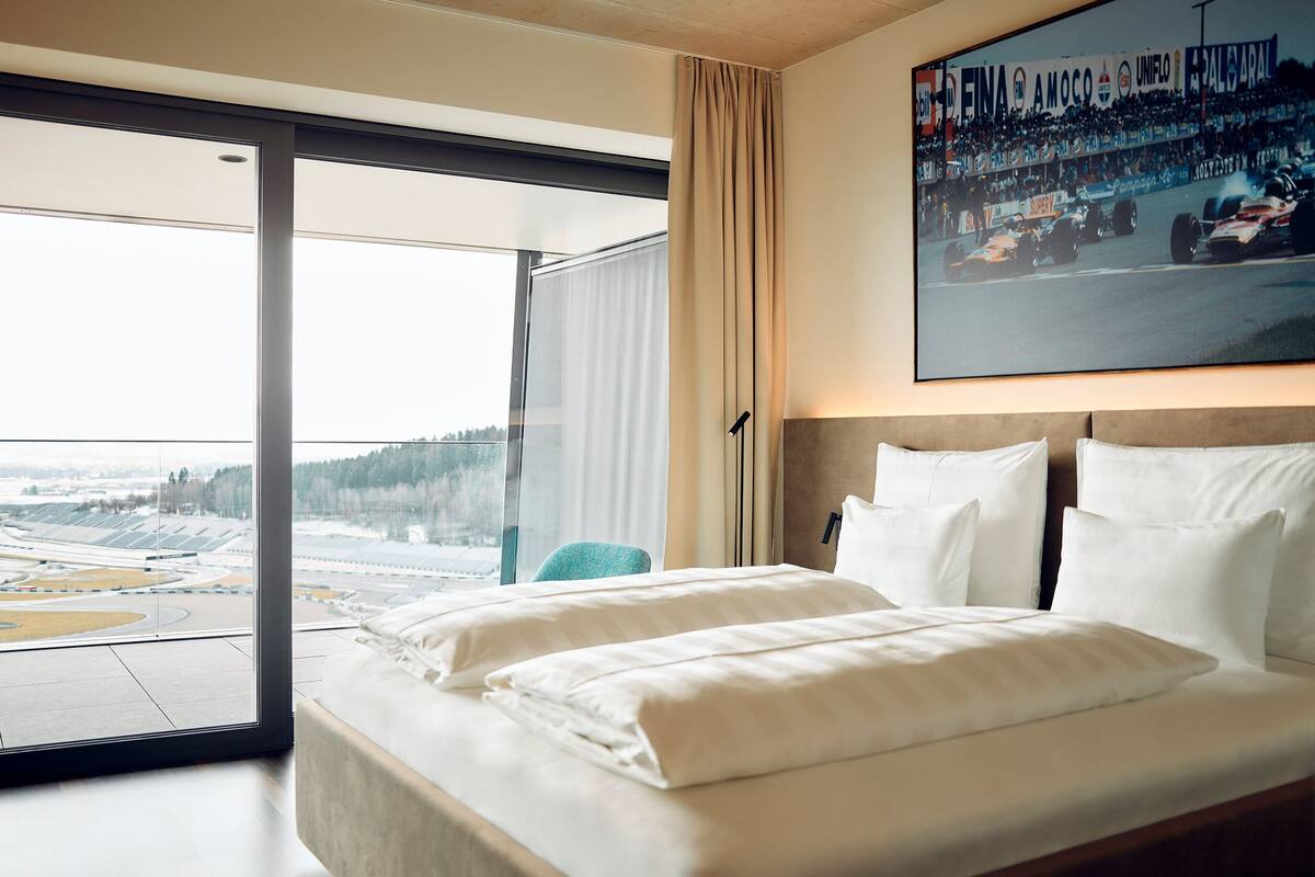 Une chambre d’hôtel avec un grand lit, une vue sur un paysage enneigé et une affiche de voiture de course au mur.