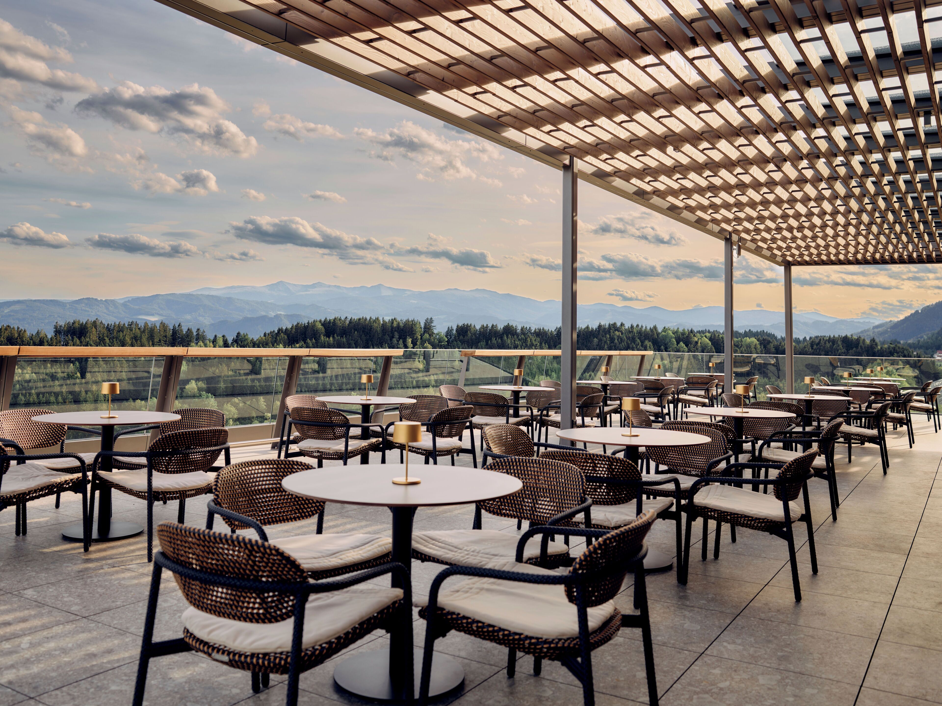 Terraza al aire libre con mesas redondas y sillas de mimbre, con vistas a montañas distantes.