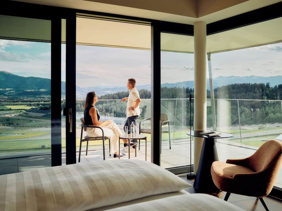 Habitación de hotel con balcón grande, una cama, una silla y una mesa.