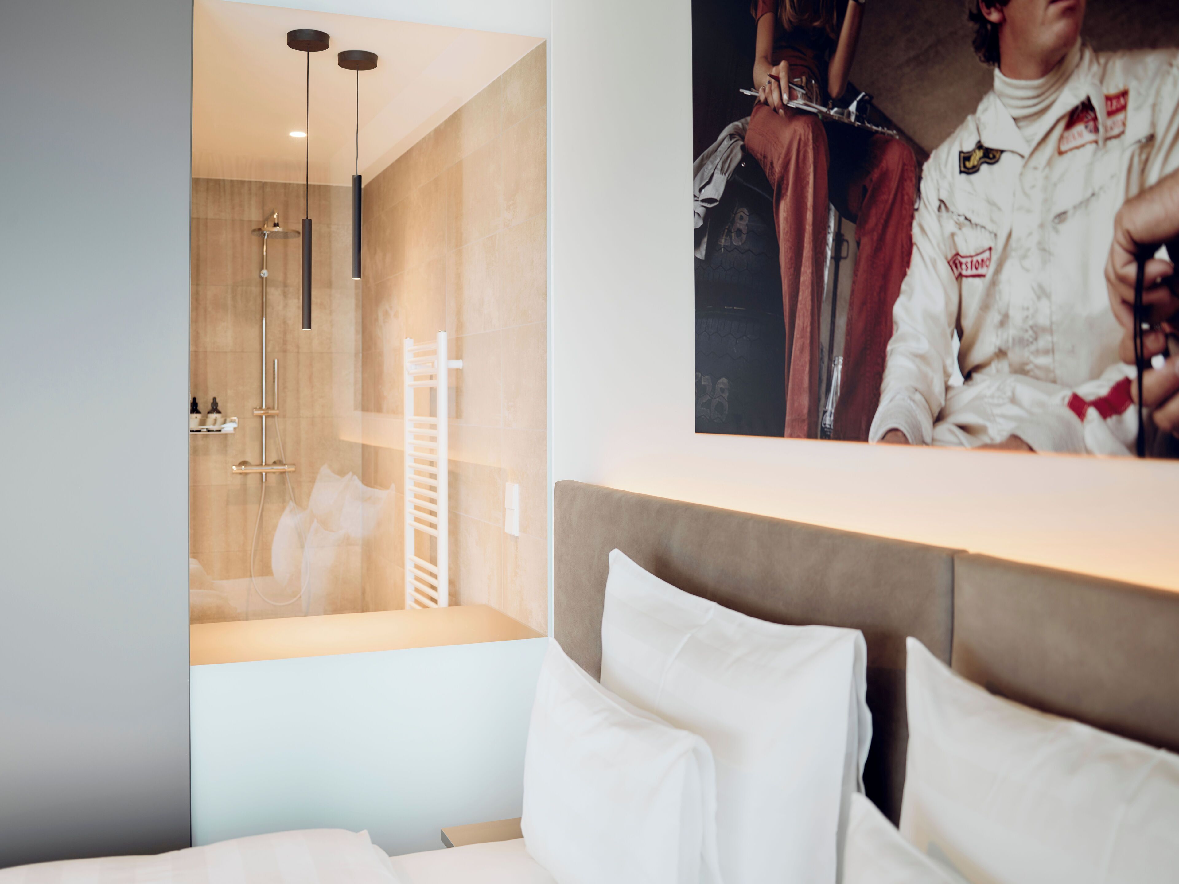 Una camera d'albergo moderna con un letto grande, zona doccia con porta in vetro e un quadro appeso al muro.