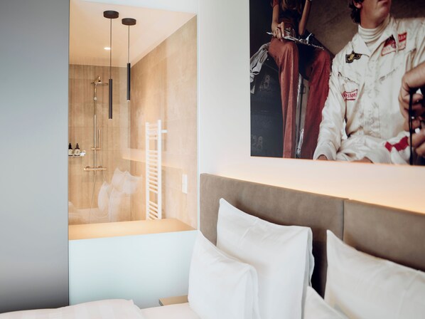Habitación de hotel moderna con una cama grande, zona de ducha con puerta de cristal y un cartel en la pared.