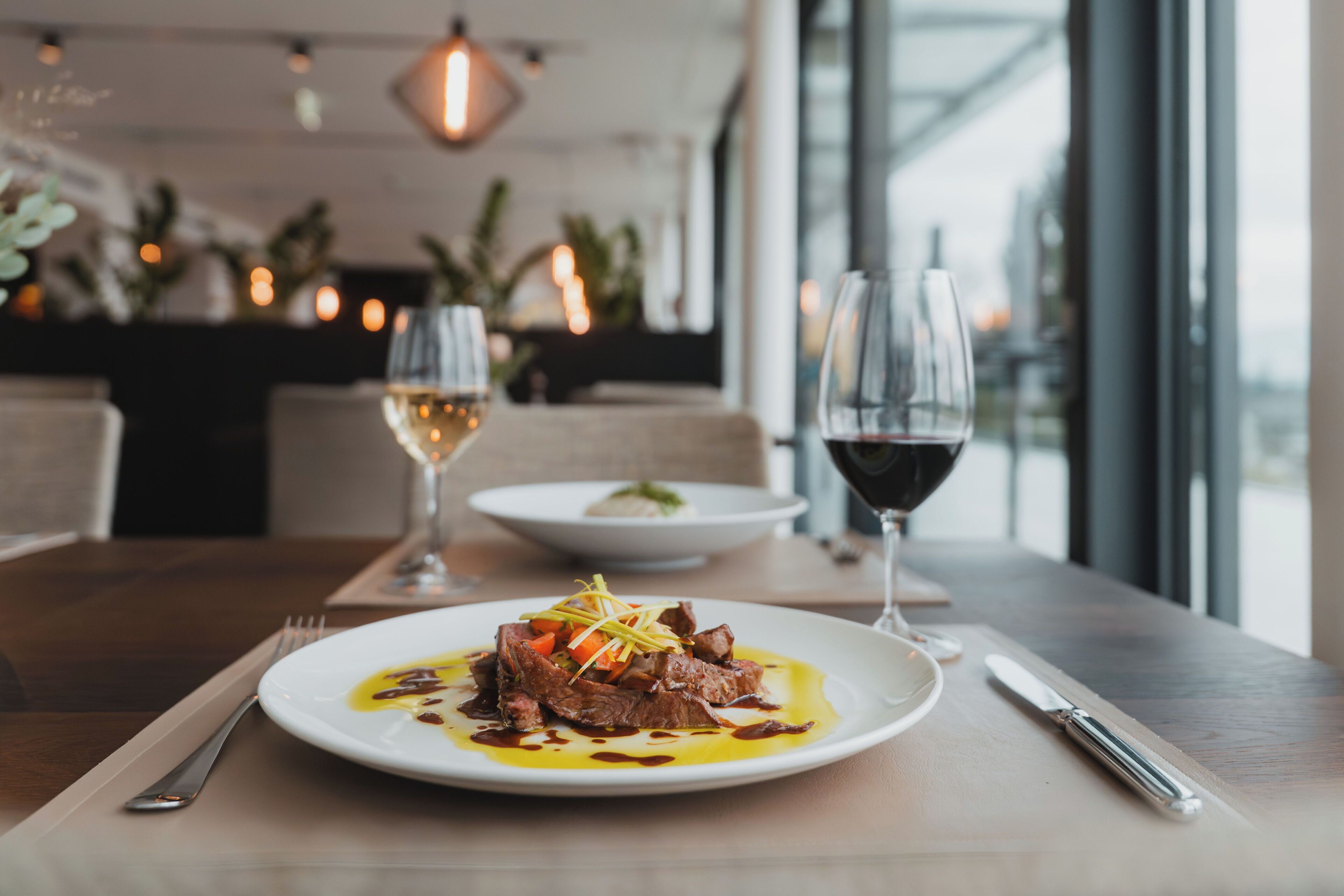 Une table à manger avec une assiette de nourriture, deux verres de vin, une fourchette et un couteau posés sur une serviette.