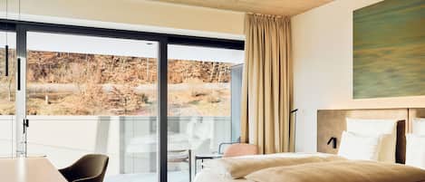 Ein modernes Hotelzimmer mit einem großen Bett, einem Schreibtisch und Blick auf eine natürliche Landschaft durch eine Schiebeglastür.
