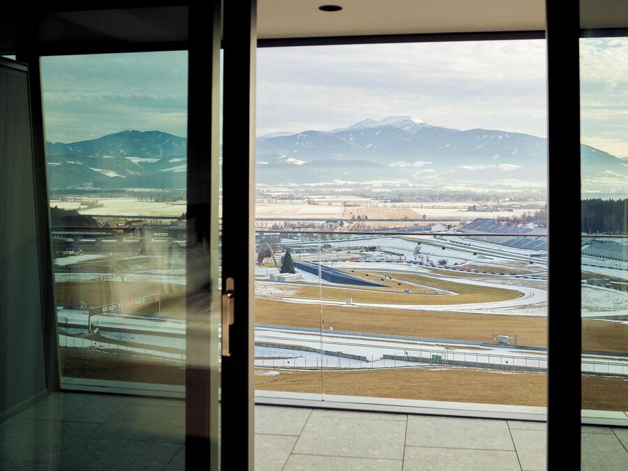 A view from a room with large windows overlooking a snowy landscape with mountains and a complex of buildings.