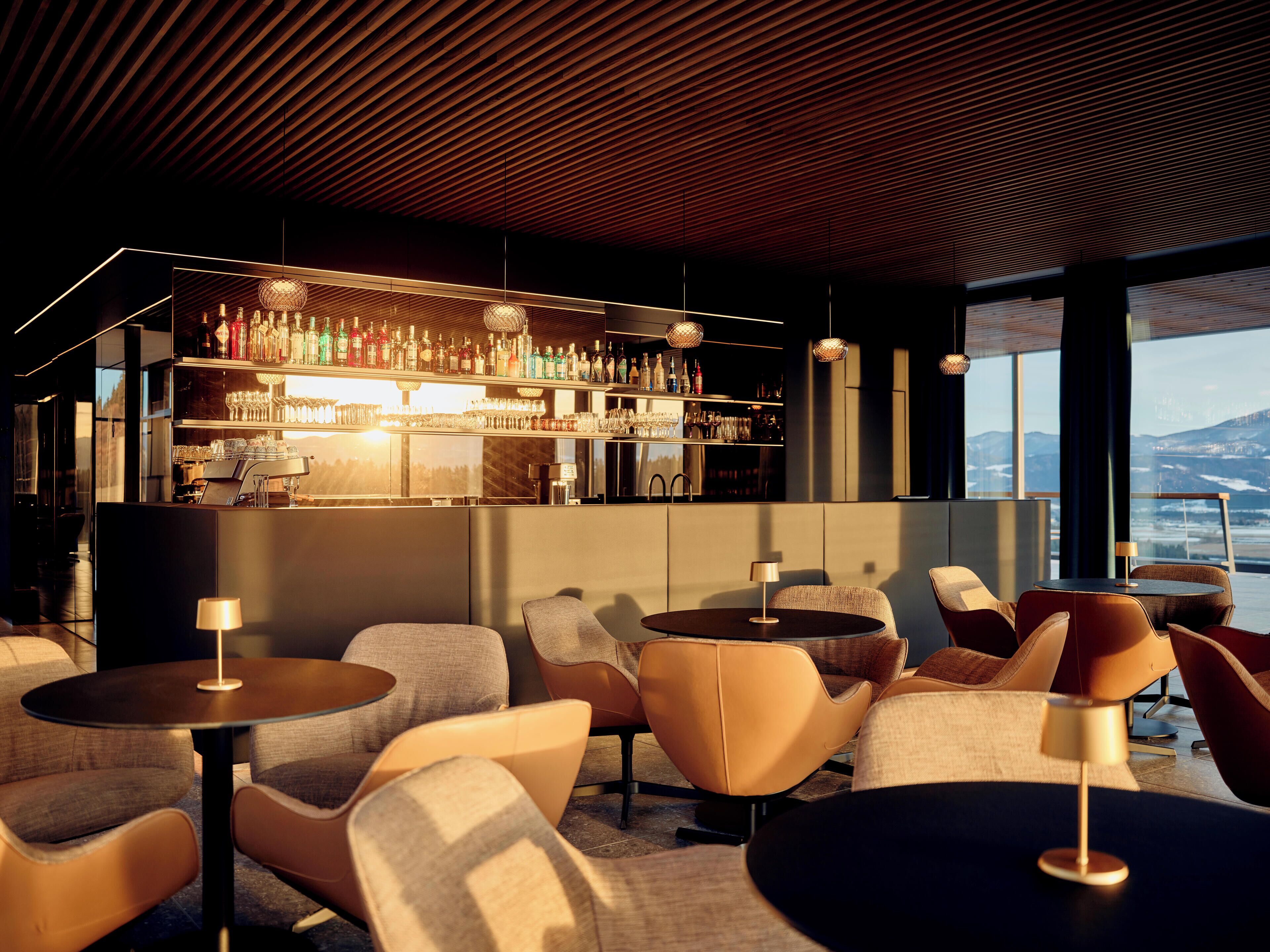 A modern bar area with seating, a bar counter with bottles, and a view of the mountains.