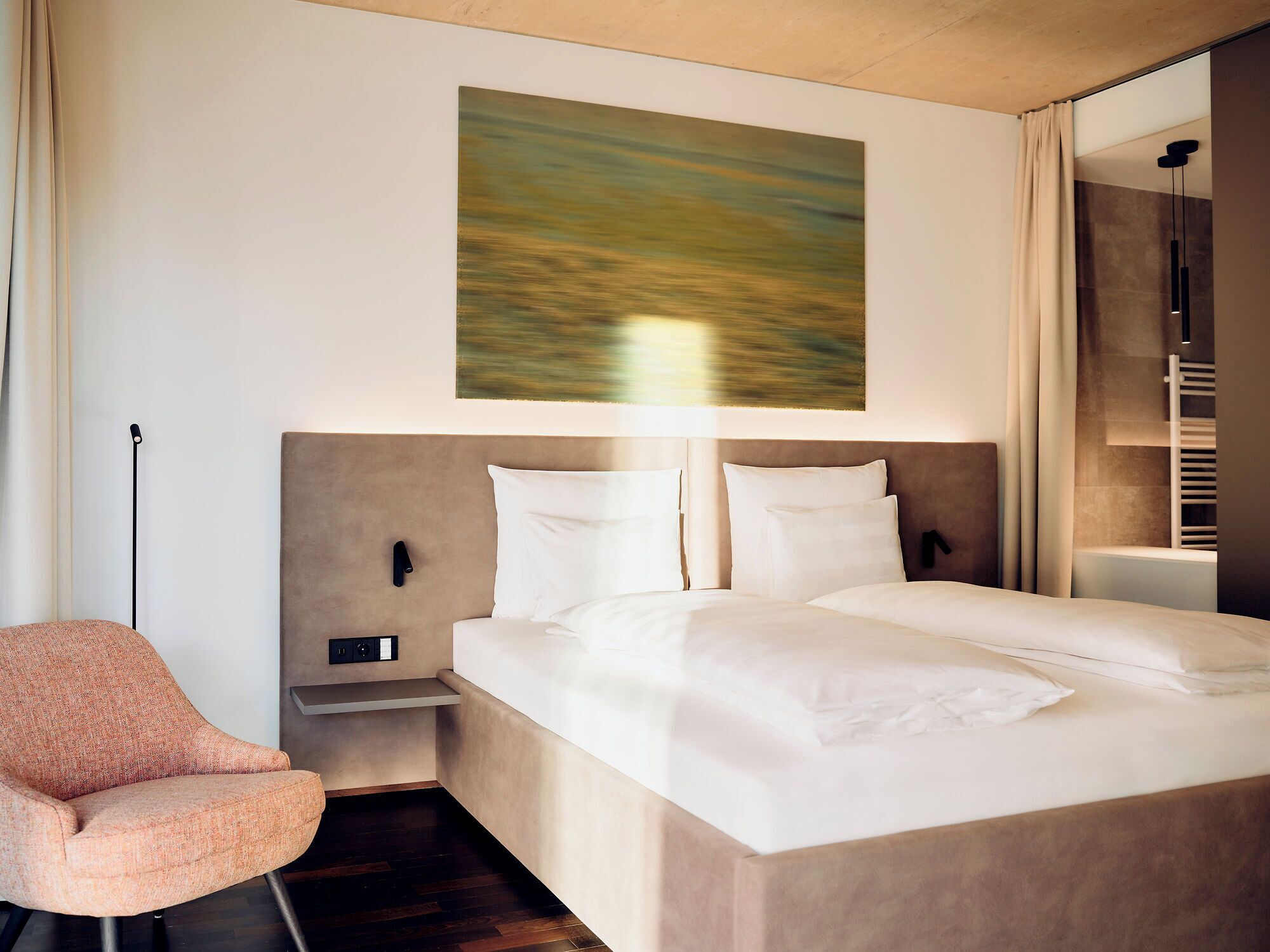 Ein modernes Hotelzimmer mit einem großen Bett, einem Nachttisch, einem Sessel und einem Bild an der Wand.