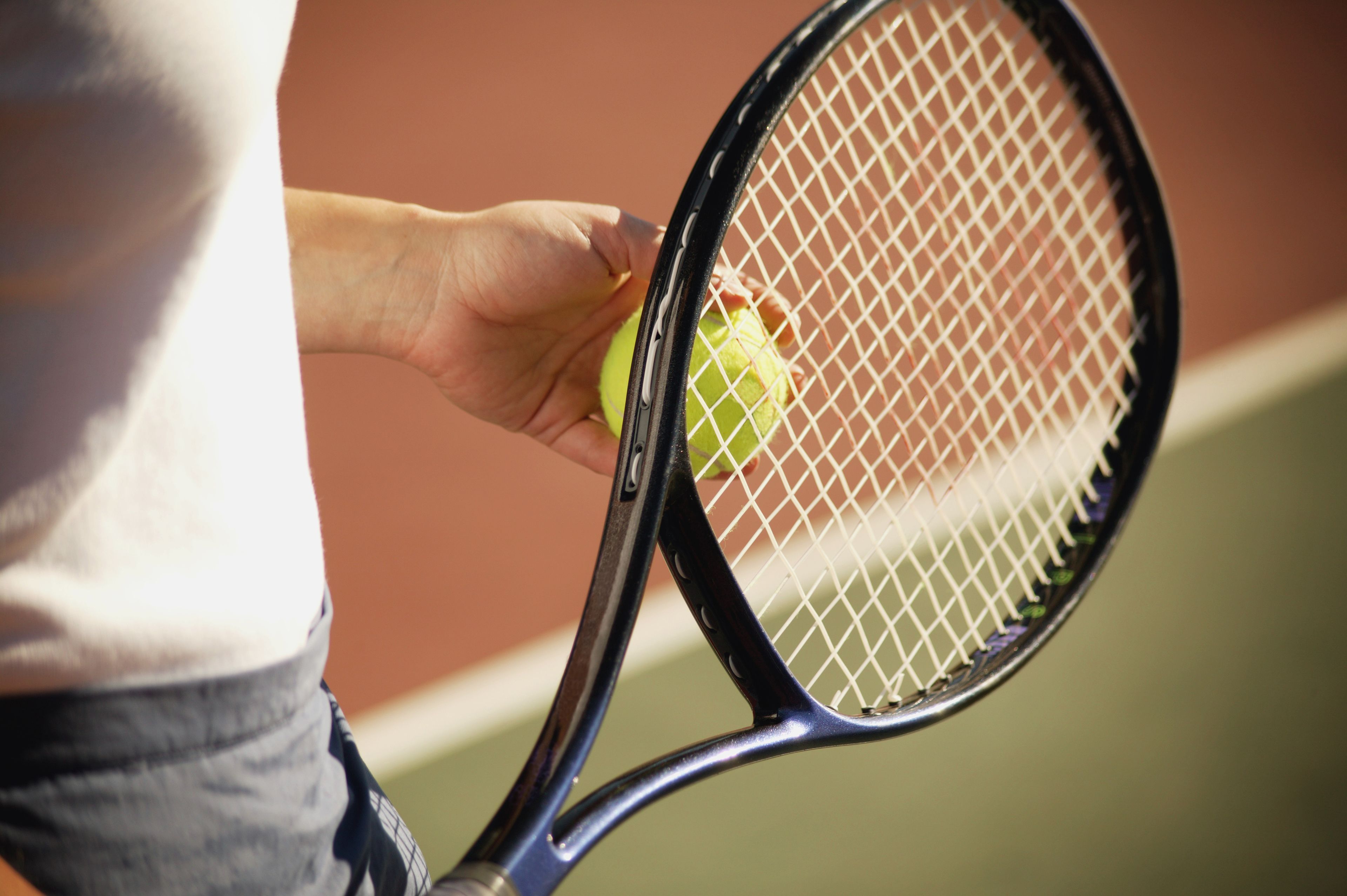 Primer plano de una raqueta de tenis con una mano sosteniendo una pelota.
