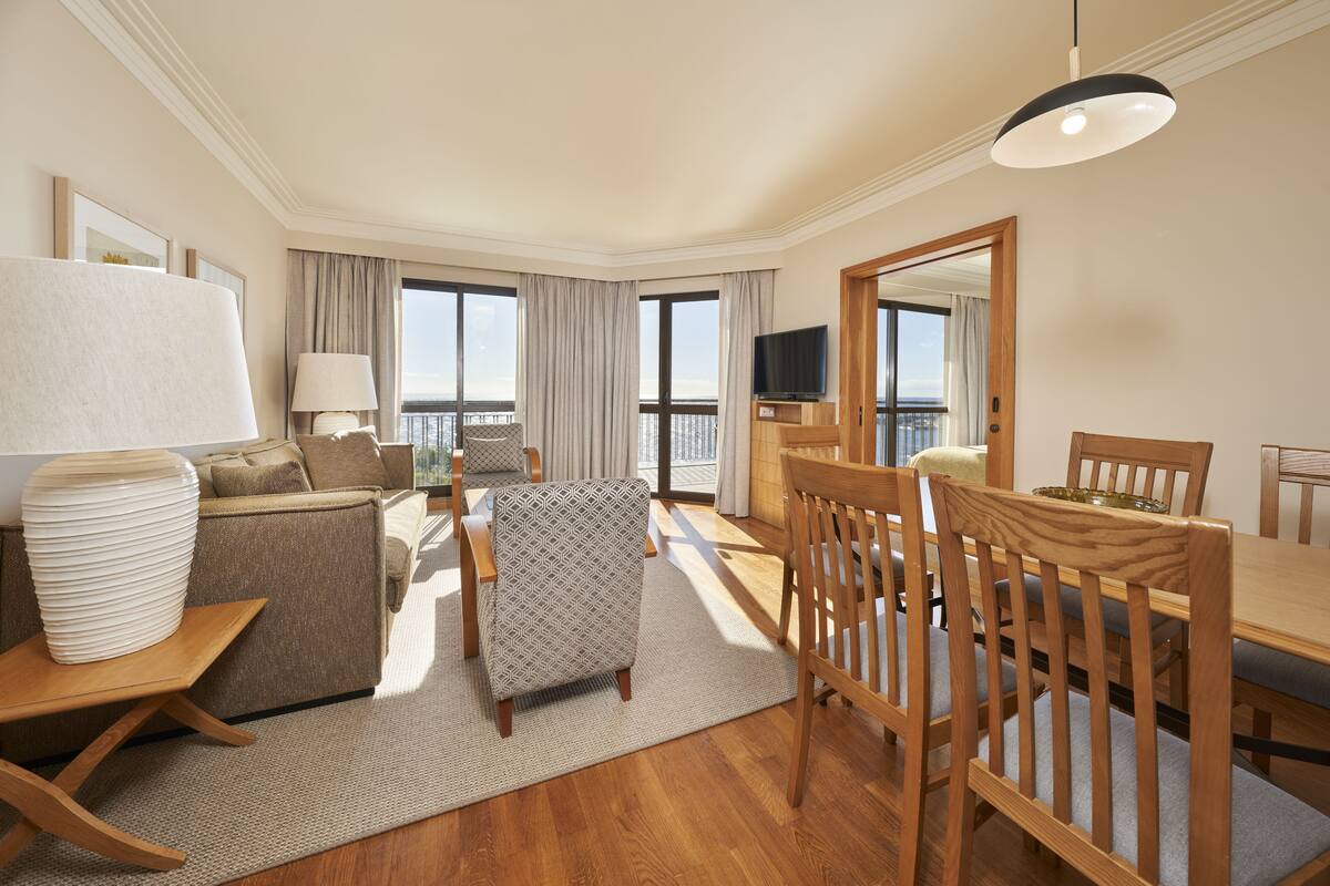 Habitación de hotel con sofá, sillón, mesa de comedor y televisión.