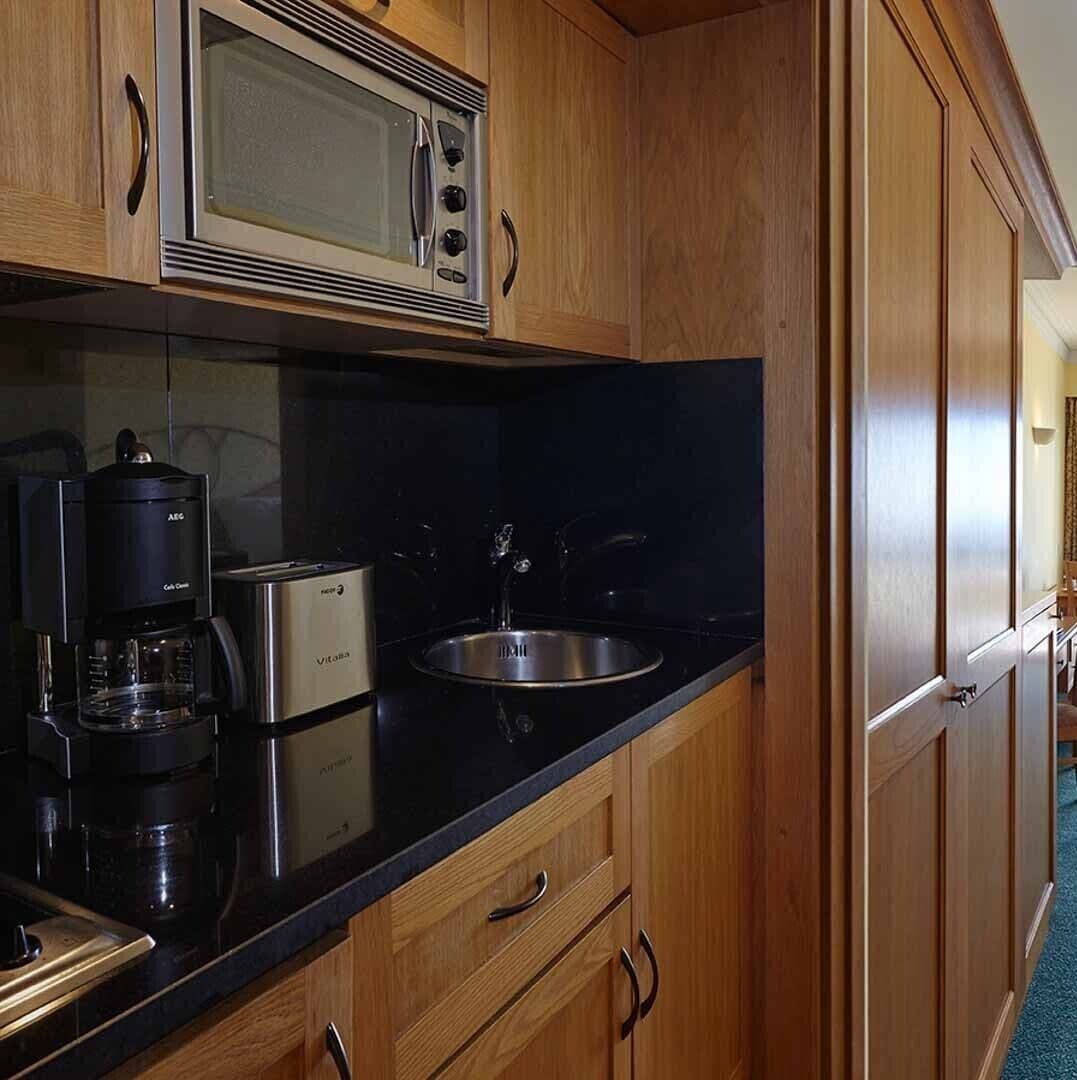 Una cocina con armarios de madera, un lavamanos de acero inoxidable, un microondas y una cafetera.