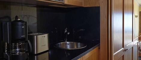 Una cocina con armarios de madera, un lavamanos de acero inoxidable, un microondas y una cafetera.