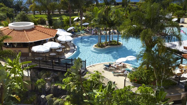 Un resort con varias piscinas, palmeras y vista al océano.