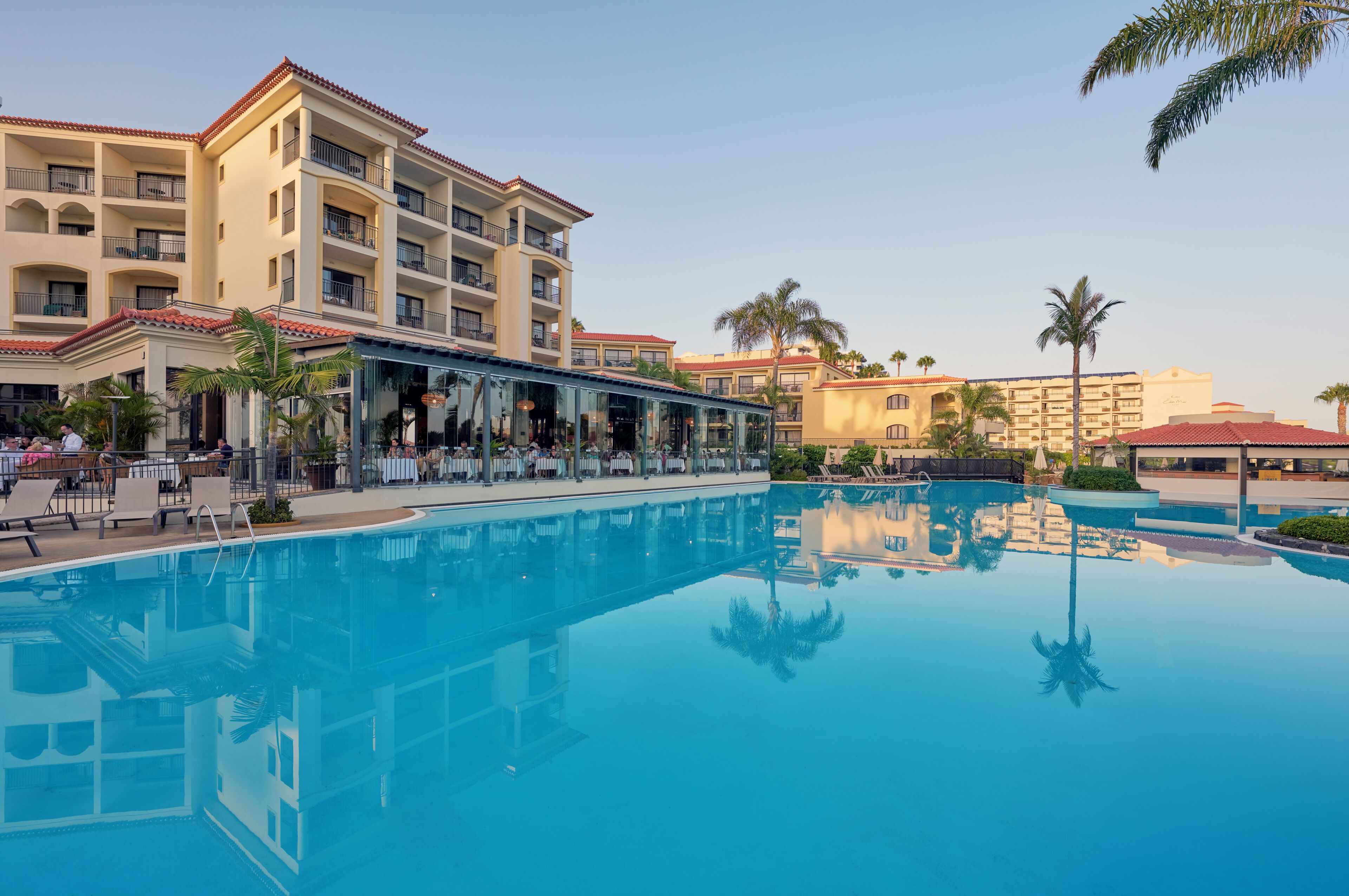 A hotel with a large swimming pool, outdoor seating, and multiple balconies.