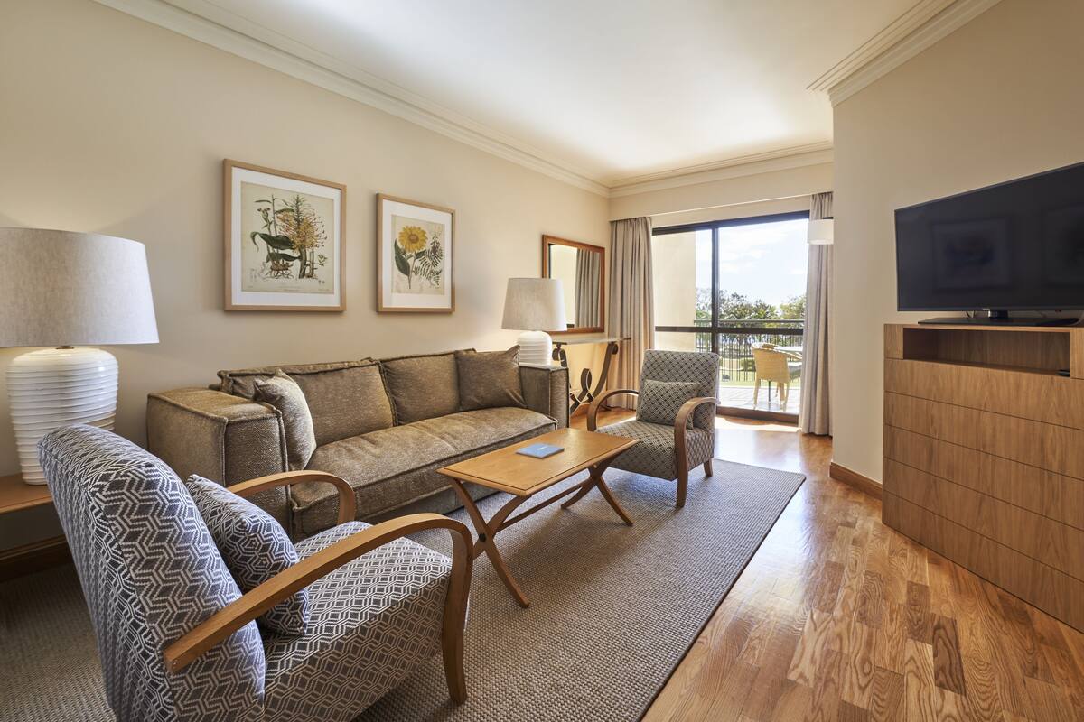 Habitación de hotel con sofá, sillones, una mesa de centro, televisor y obras de arte en las paredes.