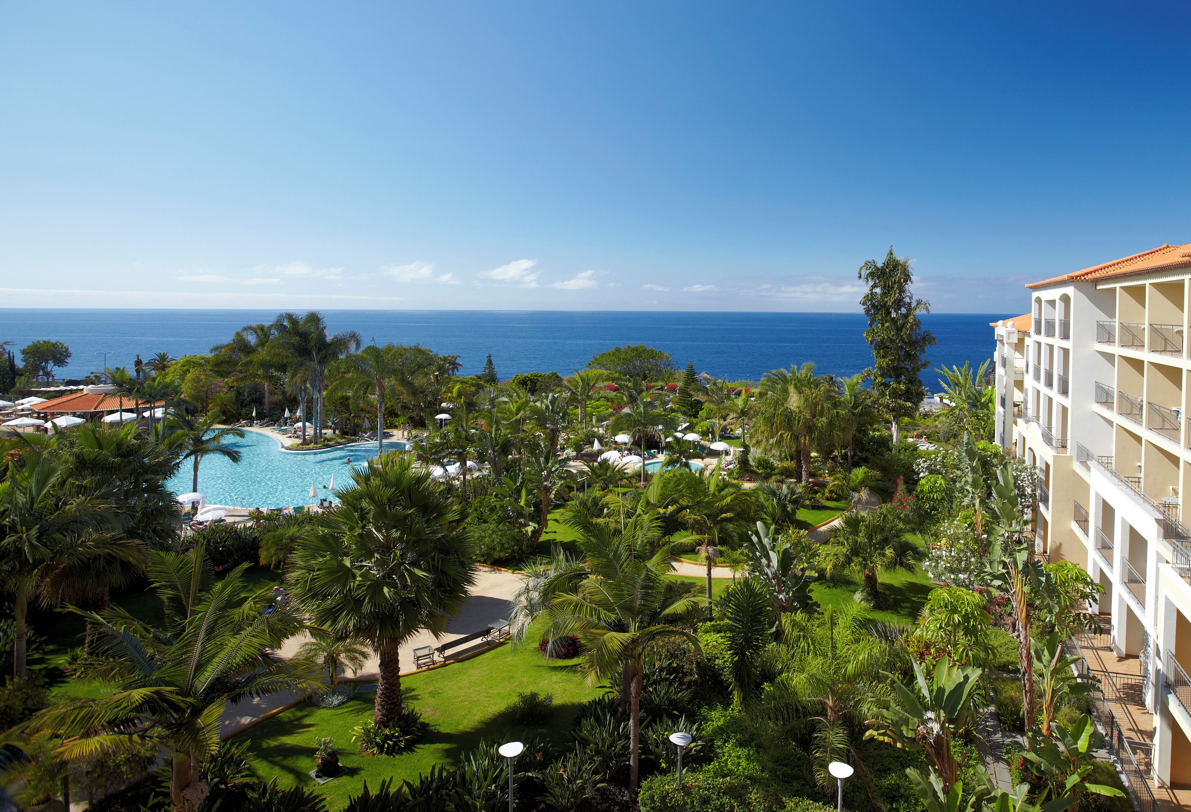 A resort with a swimming pool, lush greenery, and a view of the ocean.