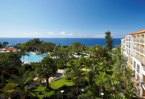 Een resort met een zwembad, weelderige begroeiing en uitzicht op de oceaan.