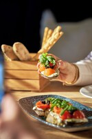 A person holding a food item with a wooden background and a plate with food in the foreground.