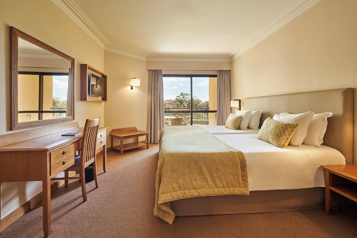 Een hotelkamer met een bed, een bureau, een stoel, een televisie en uitzicht op een balkon.