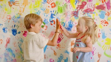 Two children engaging with a wall covered in colorful handprints.