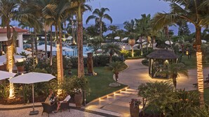 Un resort con asientos al aire libre, palmeras, piscina y un pabellón.