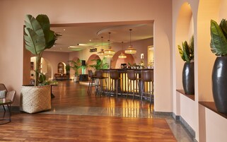 A modern bar area with wooden flooring, bar stools, and ambient lighting.