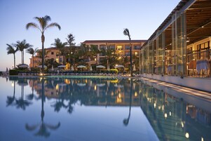 A hotel pool area with a reflection of palm trees and a building.