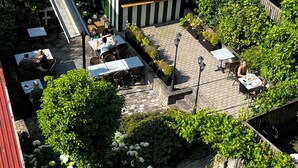 Un patio al aire libre con mesas y sillas, rodeado de vegetación y un pequeño edificio con techo inclinado.