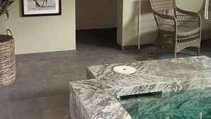 Una habitación con una mesa de mármol, una silla de mimbre, cuadros en la pared y una lámpara fijada a la pared.