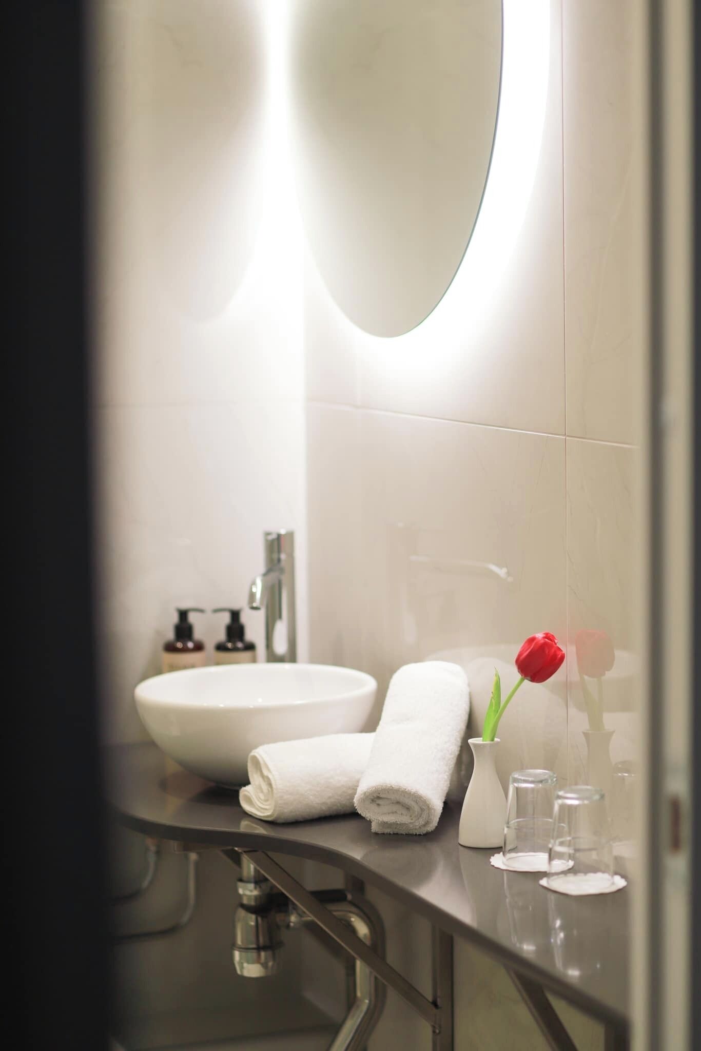 A modern bathroom with a white sink, a mirror, and a red rose on the counter.