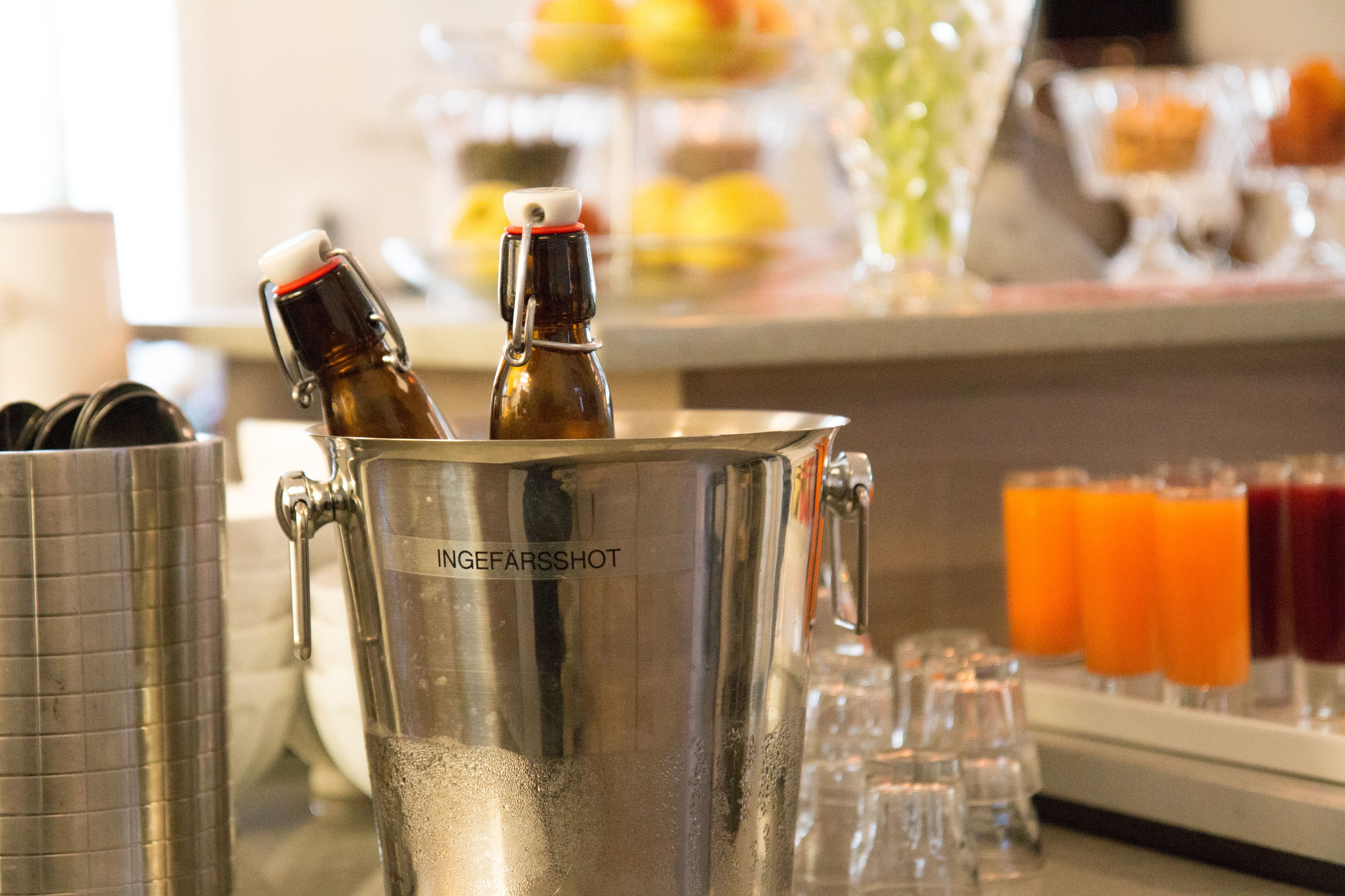 A stainless steel beverage dispenser with two bottles, a tray of glasses, and a selection of juices.