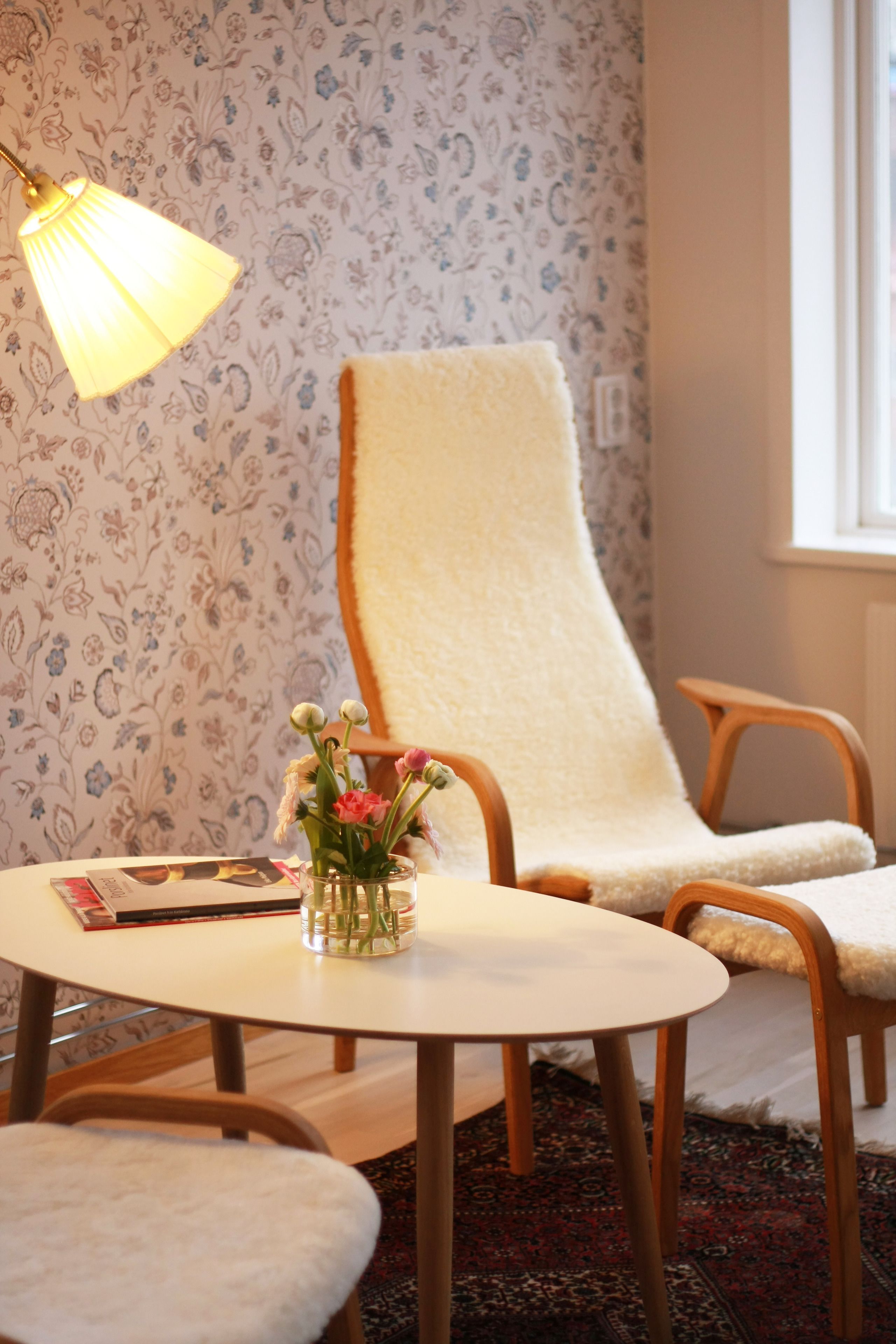 Ett rum med ett runt bord, två stolar, en lampa och en blommig tapet.