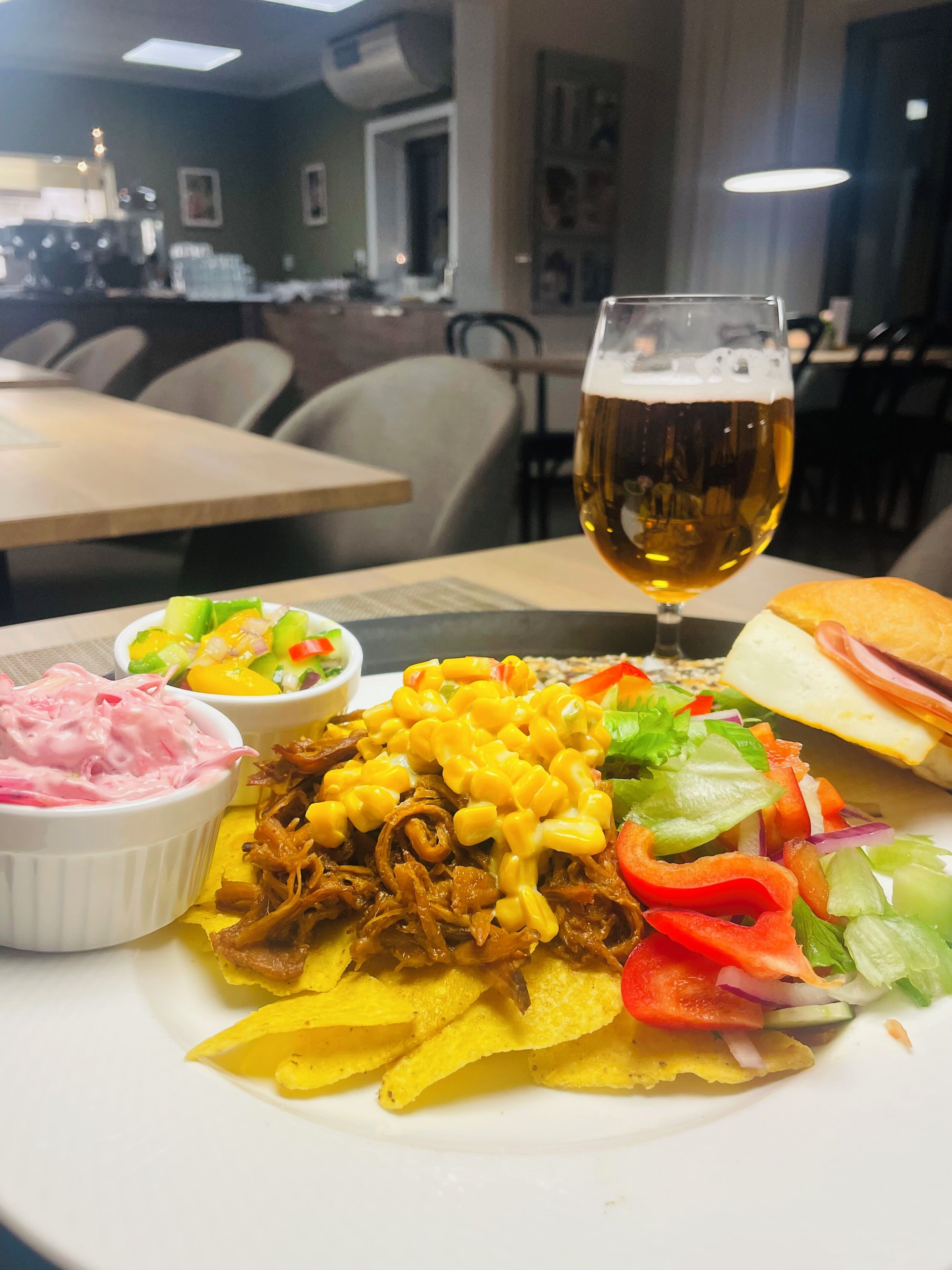 A meal with pulled pork, corn, and a salad, along with a glass of beer and a sandwich.