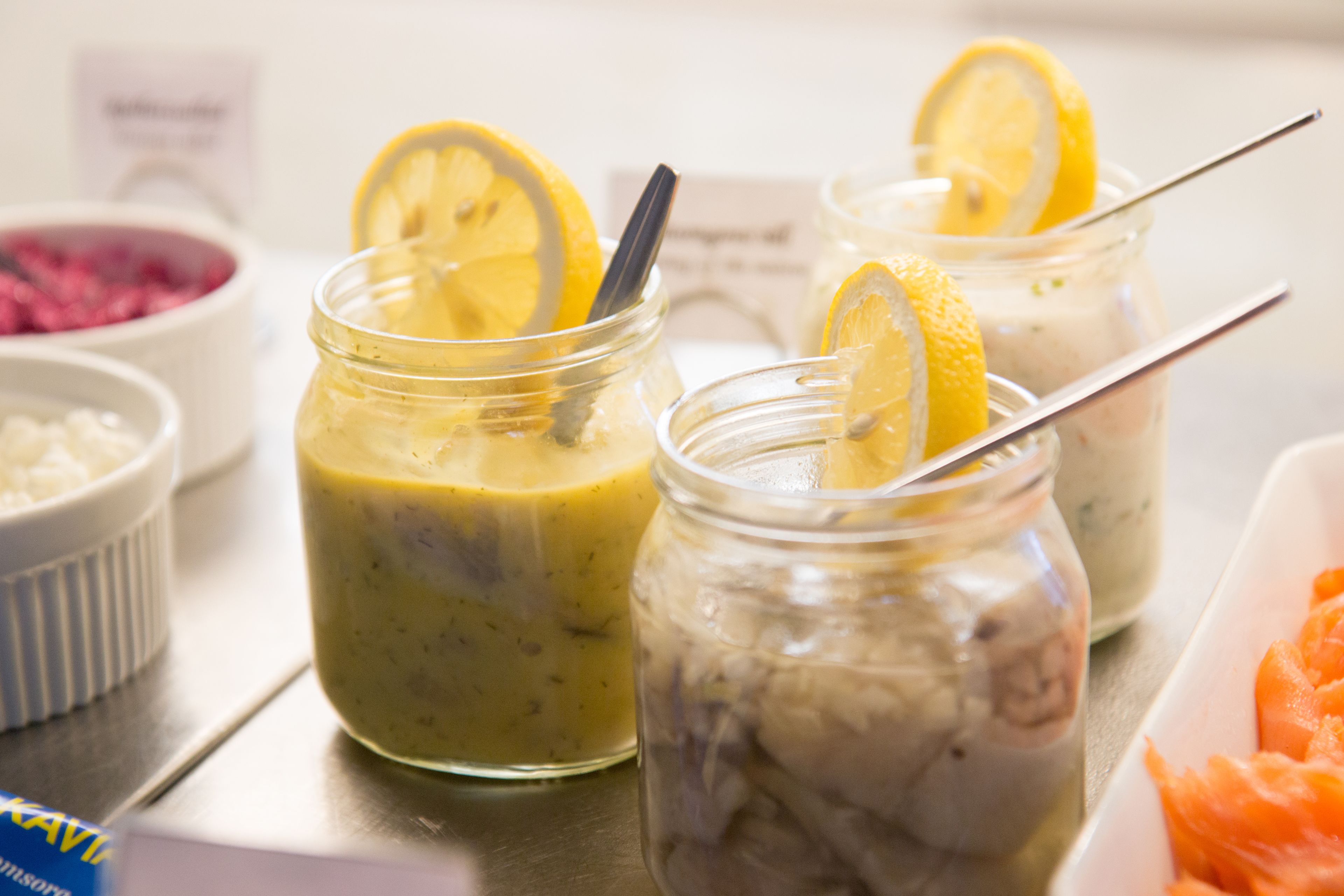 Three glass jars with lemon slices and a spoon, a bowl of red food, and a plate of salmon.