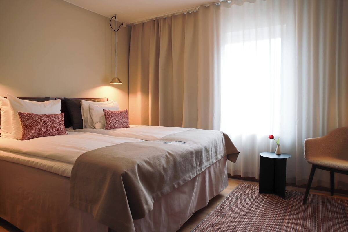 Ein Hotelzimmer mit einem großen Bett, einem Beistelltisch mit einer Vase und einem Sessel.
