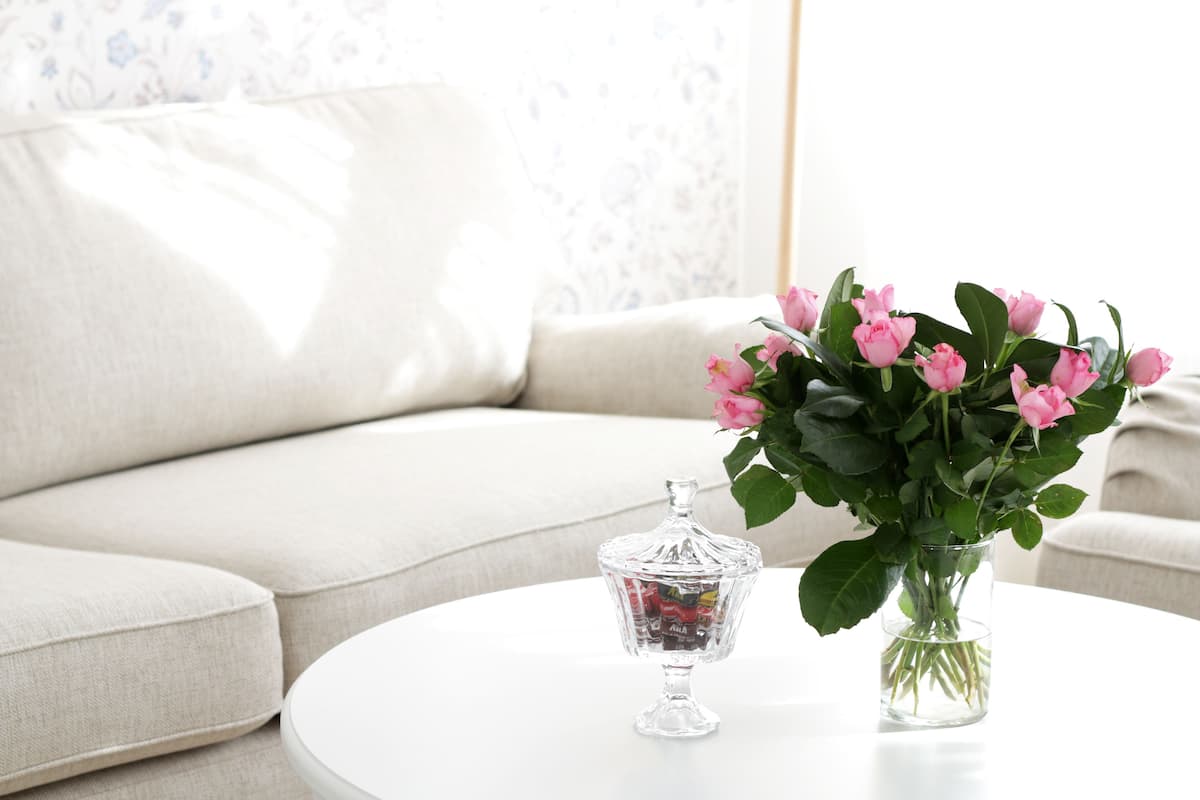 Ein weißer runder Tisch mit einem Glasbehälter und einer Vase voller rosa Blumen.