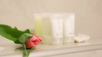 A bathroom counter with three bottles of body lotion and a pink rose.
