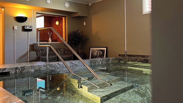 Un área de spa con una piscina de mármol, una escalera de madera y una recepción.