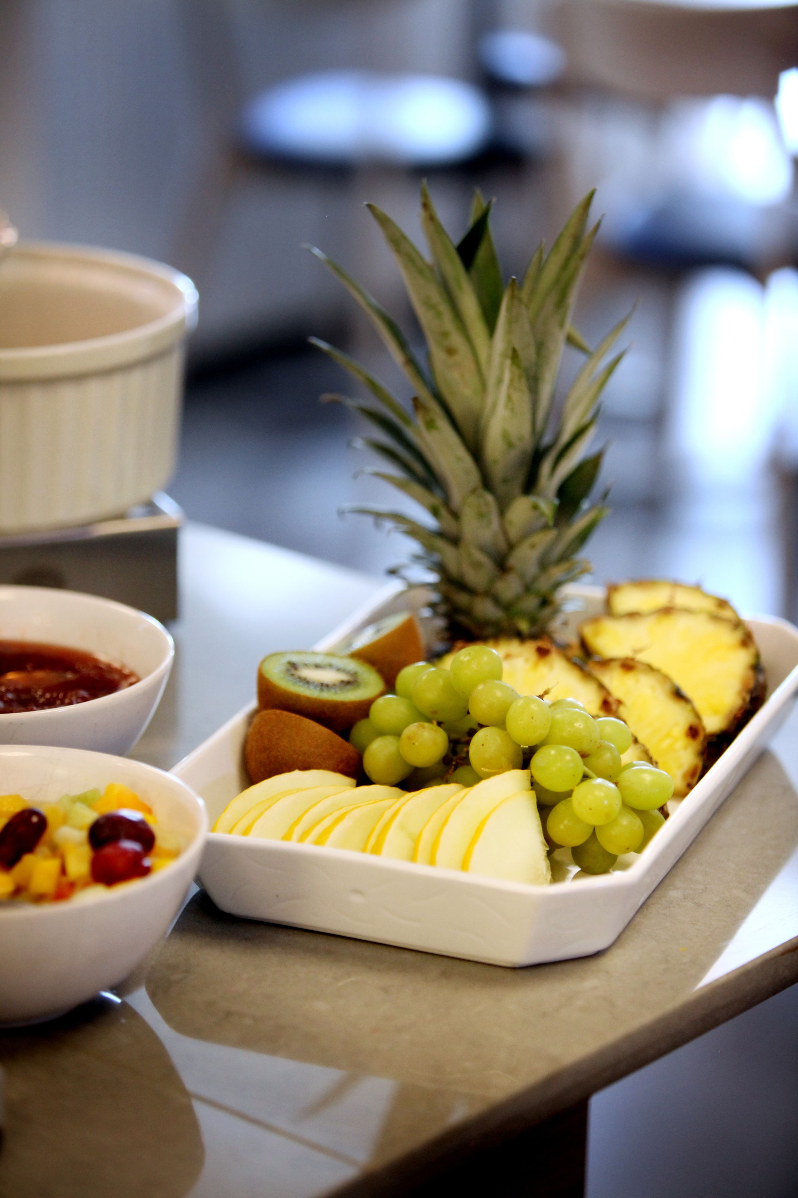 A tray of sliced fruits including pineapple, kiwi, grapes, and apples, along with a bowl of mixed fruit.