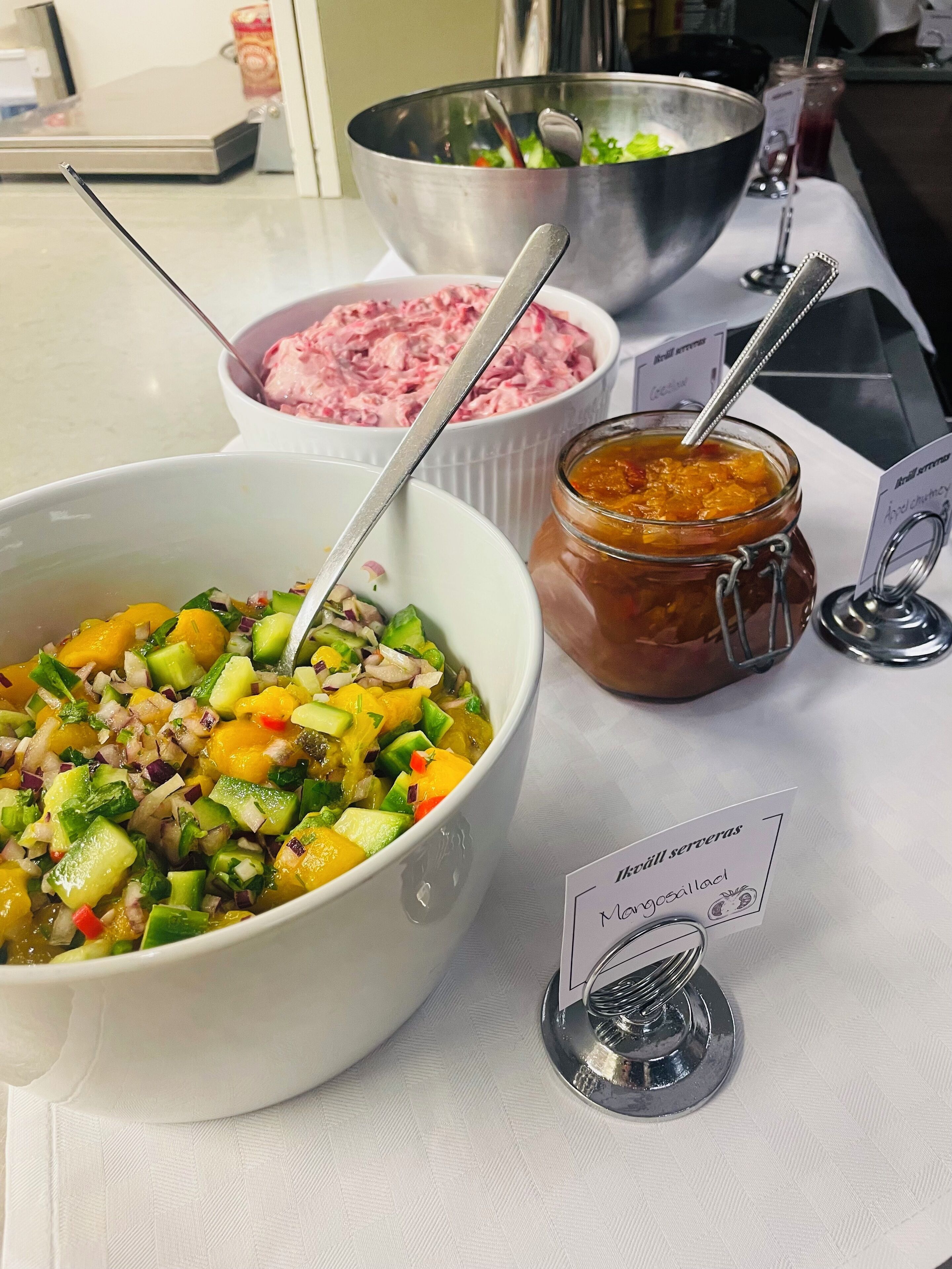 A buffet table with various dishes including a bowl of mixed vegetables, a jar of sauce, and a bowl of pink salad.