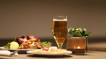 Ein Tisch mit einer Mahlzeit aus Salat, einem gekochten Ei und einer Scheibe Toastbrot mit Butter und Marmelade, dazu ein Glas Bier und eine angezündete Kerze.