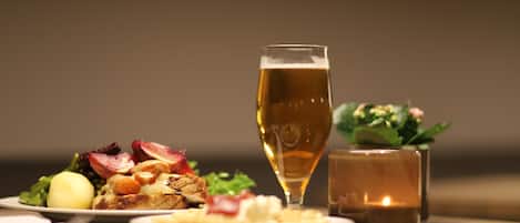 Una mesa con comida que incluye una ensalada, un huevo duro, una tostada con mantequilla y mermelada, acompañada de una cerveza y una vela encendida.
