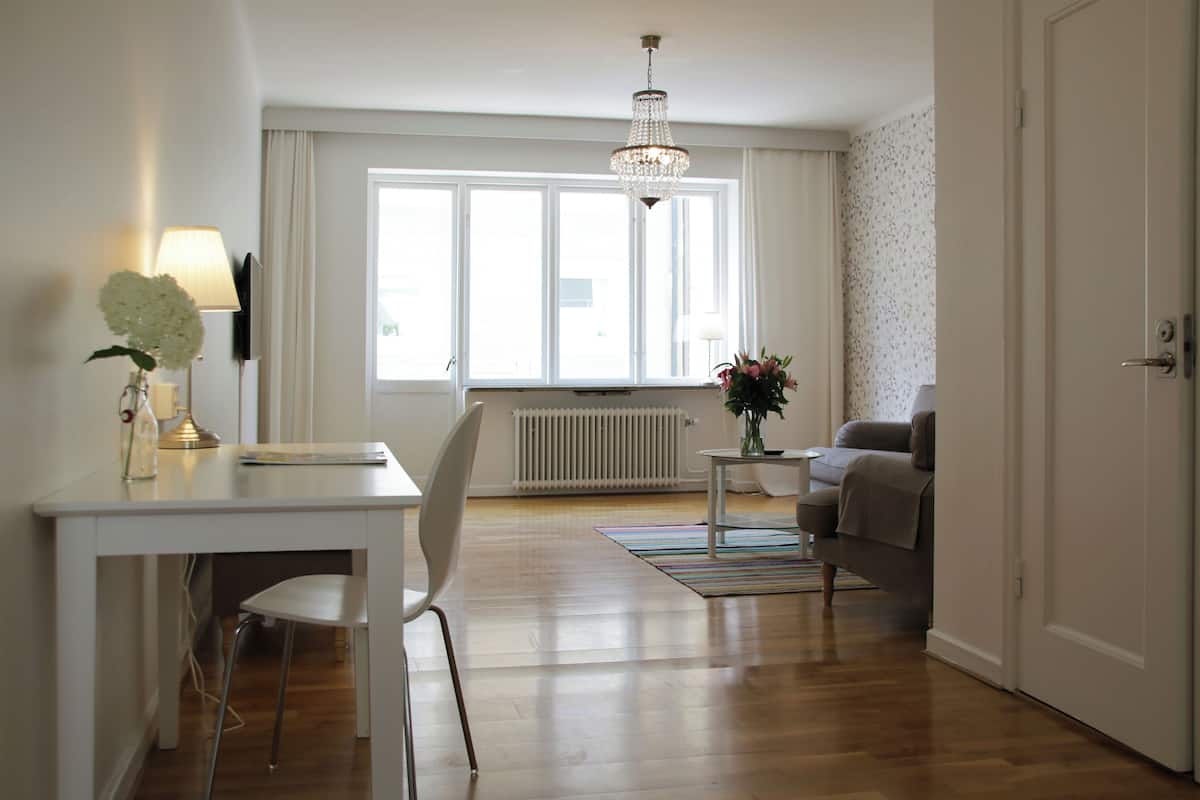 Ein modernes Wohnzimmer mit einem weißen Tisch, einem weißen Sessel, einer Couch, einem kleinen Beistelltisch mit einer Vase und einer Heizung.