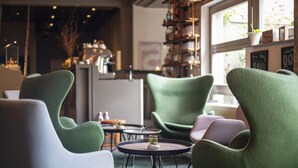 A modern interior with green and white upholstered chairs, a small round table with a plant, and a kitchen area in the background. - BIG MAMA Berlin (Berlin)