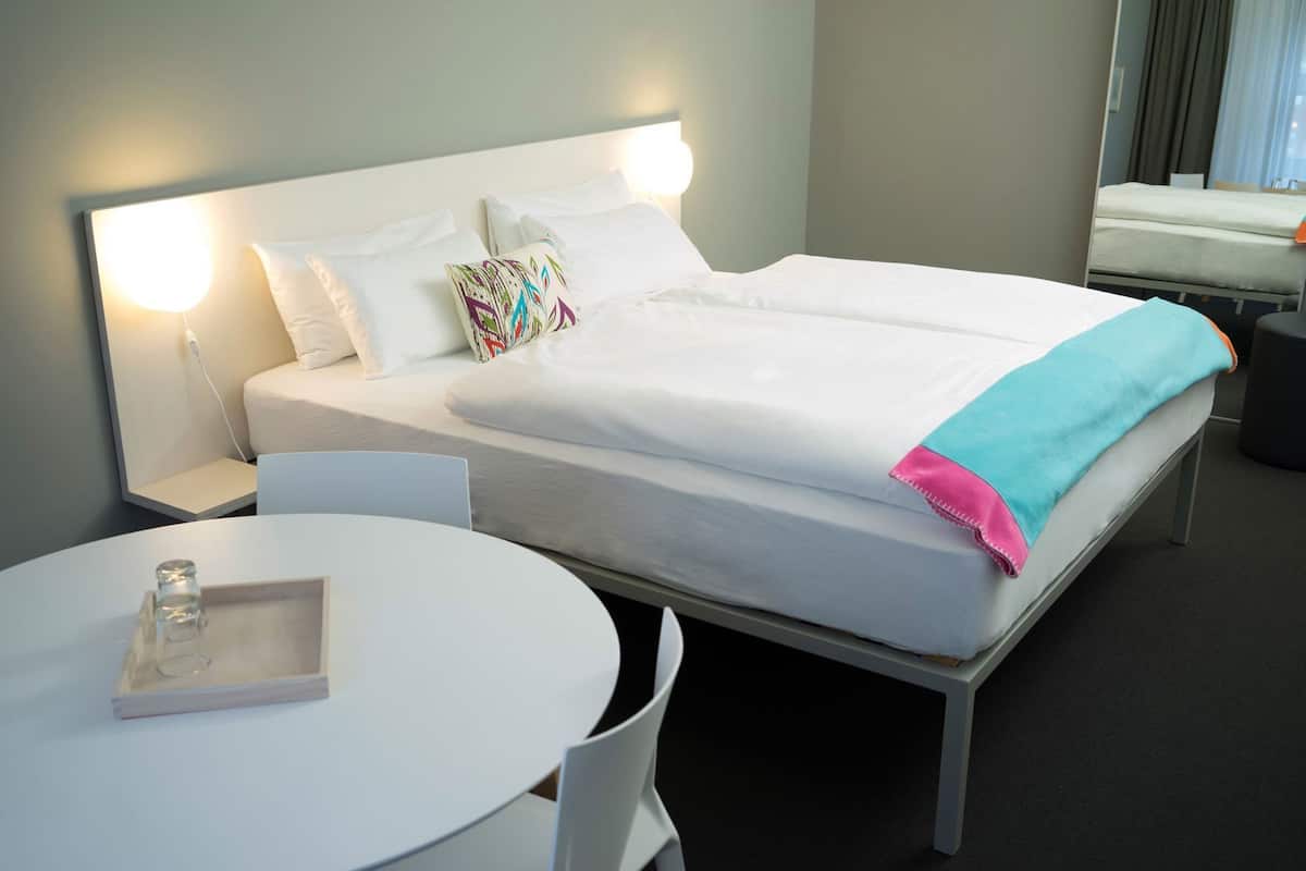 A hotel room with a bed, bedside tables, a round table, and a chair.