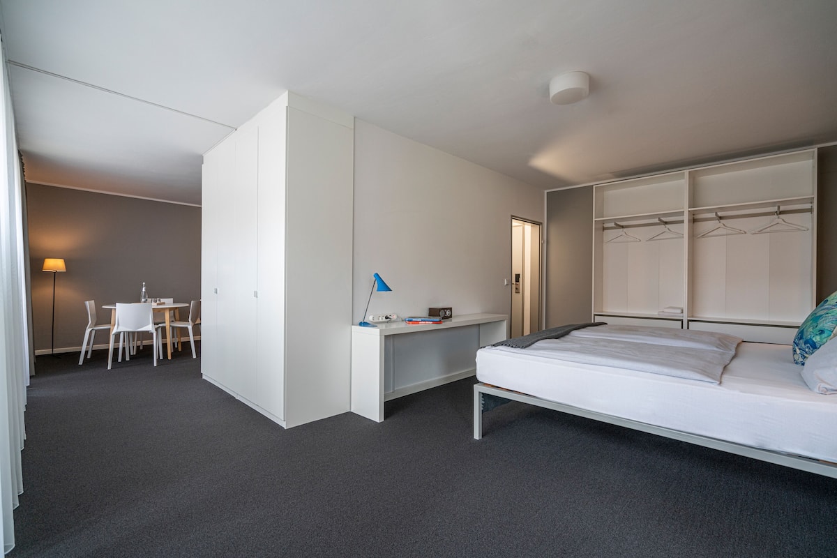 A modern hotel room with a bed, a desk, and a chair.